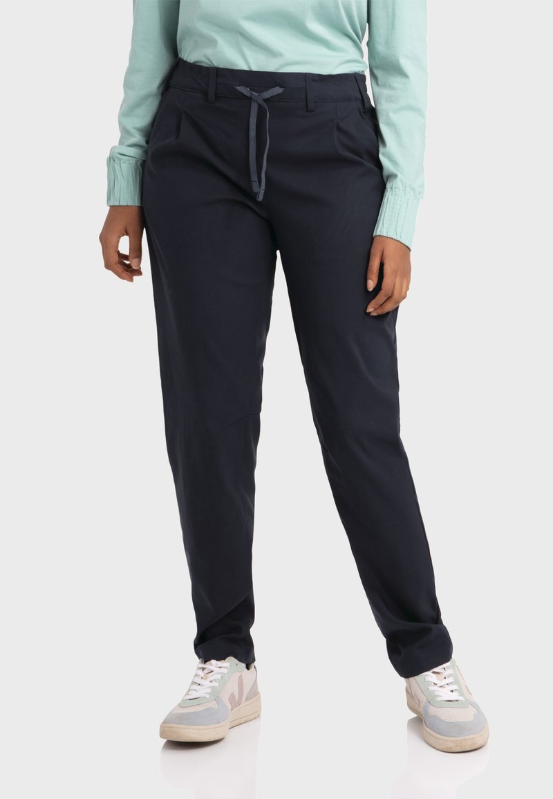 Dunkelblaue Freizeit-Hose mit einem Kordelzugbund, zwei Vordertaschen und einer schmal zulaufenden Form. Kombiniert mit hellen Sneakern.