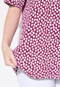 Blusa de manga corta en un magenta profundo con un estampado floral de margaritas blancas. La tela parece ligera con una textura suave.