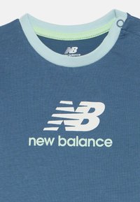 Blauwe New Balance-shirt met lichtblauwe kraagafwerking en witte New Balance-logo en tekst gecentreerd op de borst.