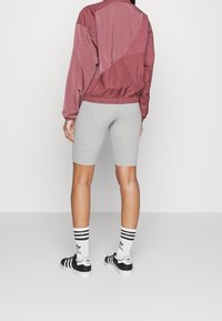 Röd satin bomberjacka med elastisk fåll, grå cykelbyxor, svarta och vita randiga strumpor och svarta sneakers med vita accenter.