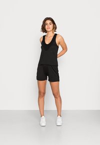 Top preto sem mangas com decote bordado, combinado com calções pretos e usado com ténis brancos. Design simples, textura suave e estilo casual.