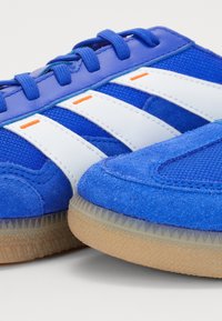 Zapatillas deportivas azules con rayas blancas y detalles naranjas, suelas de goma, material de malla y ante, y cordones azules.