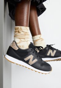 Zwarte sportschoenen met luipaardprintaccenten, bovenwerk van textuurmesh, rubberen zool, gecombineerd met beige tie-dye sokken.