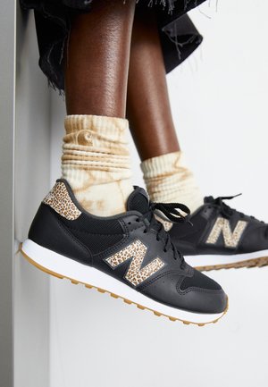 Schwarze Sportschuhe mit Leopardenprint-Akzenten, oberer Teil aus strukturiertem Mesh, Gummisohle, kombiniert mit beigen Tie-Dye-Socken.