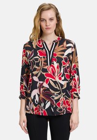 Bloes met bloemenprint in gedurfde rood-, roze- en bruintinten op een zwarte achtergrond, met een V-hals, driekwart mouwen en gathered cuffs.