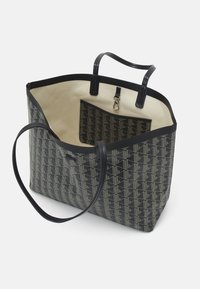 Sac cabas noir et beige avec motif géométrique, deux anses et une pochette intérieure amovible avec fermoir métallique.