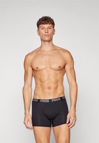 Black boxer briefs with a branded waistband, made of smooth fabric, featuring a snug fit and no visible patterns. Model is shirtless.