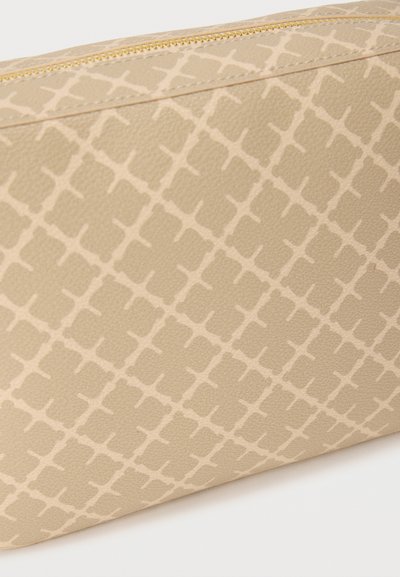 Κοντινό πλάνο μπεζ τσάντας με υφή και ελαφρύ γεωμετρικό μοτίβο διαμαντιού και ορατό χρυσό φερμουάρ κατά μήκος της πάνω άκρης.