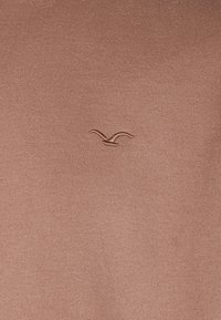 Brown cotton sweater featuring a textured finish and a small embroidered bird logo on the chest, creating a minimalist design.