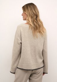 Jasno beżowy sweter o luźnym kroju, okrągłym dekolcie i czarnych wykończeniach przy mankietach i u dołu, wykonany z miękkiego, teksturowanego materiału.