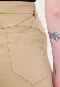 Khaki broek met een achterzak met diagonale stiksels, gemaakt van stevig materiaal, met een gladde textuur en een nette afwerking.