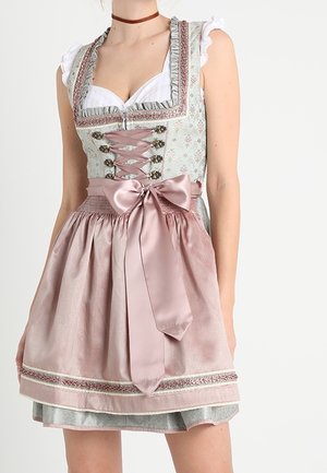 Kvinde iført en traditionel pastel dirndl-kjole med snørret liv, flæseærmer og en stor satin sløjfe bundet på forklædet i taljen.