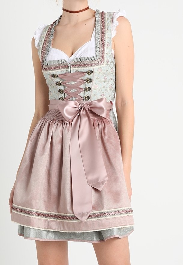 Femme portant une robe dirndl pastel traditionnelle avec corsage à lacets, manches à volants et un grand nœud en satin noué à la taille du tablier.