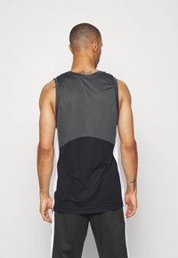 Débardeur de sport noir et gris avec une texture en maille, un design en blocs de couleur et un col rond. Coupe ample, détails minimaux au dos.