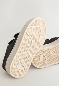 Melni apavi ar teksturētu virsmu un vienkrāsainu dizainu. Zole ir krēmkrāsā ar viļņainu protektora rakstu nodrošināšanai labākam saķerei.