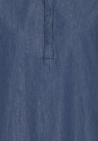 Tissu en denim bleu avec une couture verticale et un détail de patte de boutonnage courte au centre.