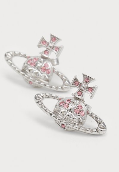 Silver earrings shaped like a planet with a ring, decorated with pink gemstones and studded pyramid details on a white background.