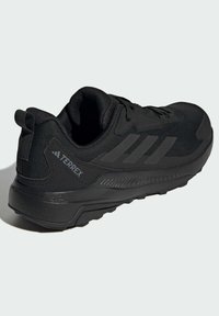 Baskets noires de sport avec une tige en maille texturée, des lacets plats et une semelle en caoutchouc. Présente un logo prominent et une languette au dos.