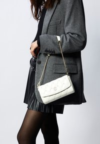 Borsa bianca trapuntata con tracolla in catena dorata e chiusura a pattina, con dettaglio del logo e texture in pelle liscia.