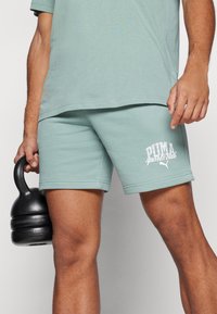 Mentolovo zelené športové šortky v m�äkkom materiáli s priliehavým strihom. Obsahujú biele logo "PUMA sports club" na ľavom stehne.