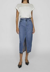 Jeanskjol med en framklippsslits, hög midja och fransad nederkant. Kombinerad med en vit kortärmad topp och svarta spetsiga ballerinaskor.