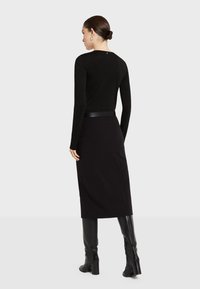 Crna bluzica dugih rukava prilagođena tijelu, uparena s crnom suknjom do koljena. Outfit uključuje elegantan kožni remen i visoke crne čizme.