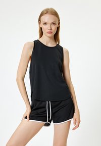 Top atlético negro sin mangas con escote redondeado, combinado con pantalones cortos negros con ribetes blancos y cordón ajustable.