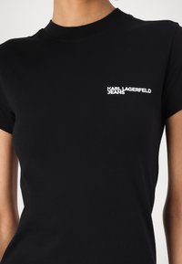 Melna kokvilnas T-kreklu ar īsām piedurknēm, uz kura kreisajā krūtīs ir balts "KARL LAGERFELD JEANS" logo. Klasisks apaļais kakls.