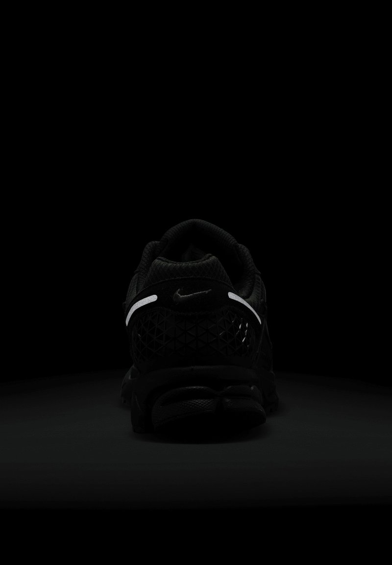 Basket noir Nike avec une tige texturée, des éléments en mesh et une bande réfléchissante le long du talon. Dispose d'une semelle rembourrée proéminente.