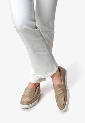 Mocassini in suede beige con punta arrotondata e dettagli di cucitura doppia, abbinati a jeans bianchi con orlo sfrangiato. Suola in gomma minimalista.