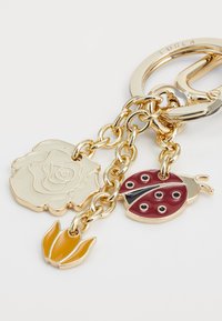 Porte-clés avec une chaîne en métal doré comportant trois breloques : une fleur blanche, une coccinelle rouge et un tulipe jaune, toutes avec des détails en émail.