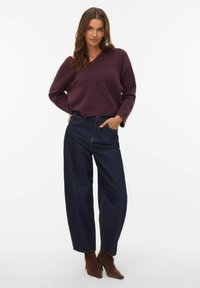 Bordo pleteni džemper s V-izrezom, uparen s visokim tamnim trapericama širokih nogavica i smeđim čizmama s potpeticom. Ležerna odjeća.