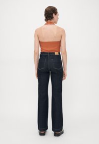 Halter-top i brent oransje stoff kombinert med høy midje mørk denim buet jeans, med kontrastsøm og to baklommer.