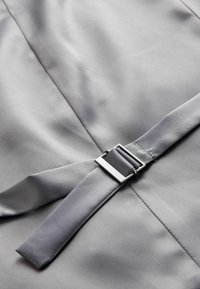 Szara tkanina o gładkiej fakturze, wyposażona w prostokątną, metalową klamrę i szeroki pasek. Delikatny połysk i wyraźne linie szwów.