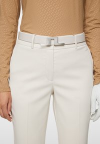 Biały pasek z metaliczną srebrną klamrą, w zestawie z kremowymi spodniami. Górna część to teksturowana beżowa koszula z długim rękawem. Minimalistyczny design.