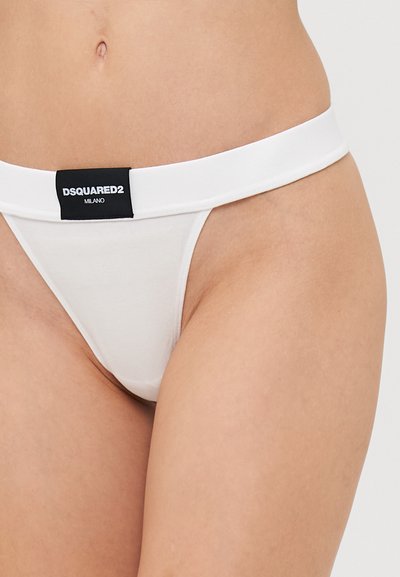 White thong with a wide elastic waistband featuring a black branded label. Soft, smooth fabric with a minimalist design.