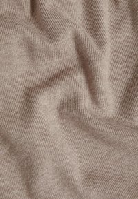 Gros plan d'un tissu tricoté côtelé beige doux avec de légères plis et une texture visible sur toute la surface.