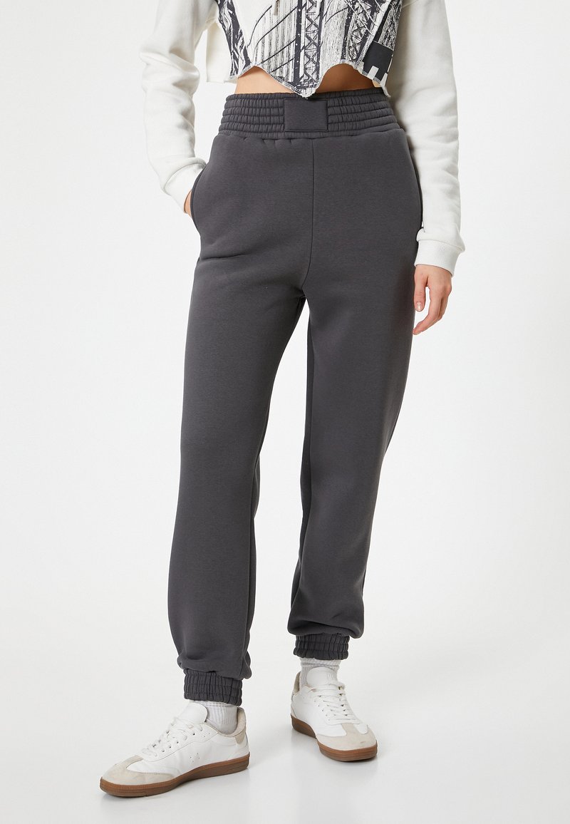 Grå joggerbukser med en tekstureret talje, sidelommer og tapered manchetter, parret med hvide sneakers og en kort mønstrede top.
