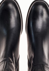 Black leather boots with a smooth surface, rounded toes, and reinforced stitching along the seams, showcasing a clean design and glossy finish.