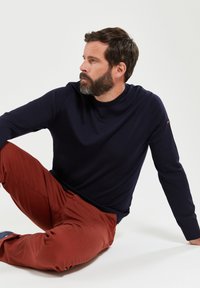 Donkerblauwe gebreide trui met een ronde hals en geribde manchetten, gecombineerd met roestkleurige pantalons. Soepele textuur en getailleerd ontwerp.