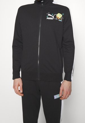 Schwarzer Puma-Trainingsanzug mit weißen Streifen, Reißverschlussjacke mit SpongeBob-Grafik auf der linken Brust und passende Hose mit Puma-Logo am linken Oberschenkel.