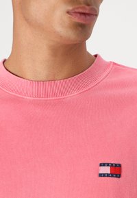Felpa rosa con colletto a costine, dotata di un piccolo logo patch multicolore "Tommy Jeans" sulla parte sinistra del petto.