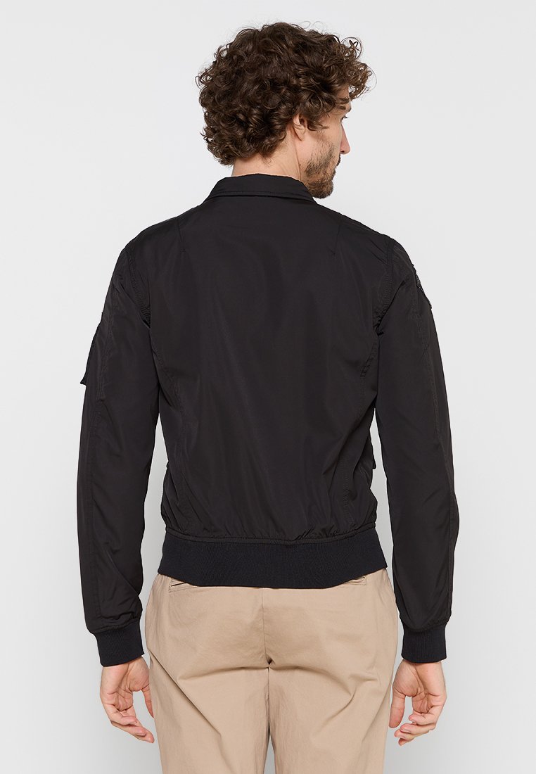 Veste bombardier noire en tissu lisse et léger. Équipée de poignets et d'ourlet côtelés, de poches latérales et d'un design de col classique.