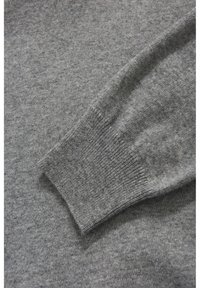 Gråt strikket sweaterstof med ribstrikkede manchetter. Teksturen er blød og har et diskret mønster samt en glat finish over hele materialet.