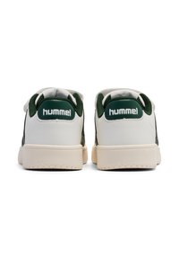 Białe sneakersy z zielonymi akcentami, z wyraźnym logo Hummel na pięcie, pokazane z tyłu. Podeszwa jest w jasnym odcieniu brązu.
