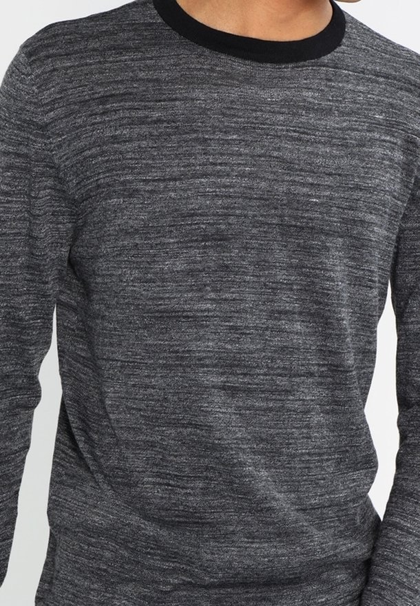 Grå långärmad tröja med subtil textur, med en svart ribbad rundhals. Tyget har ett melerat mönster som ger djup.