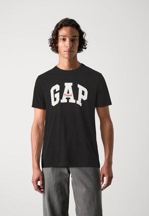 Black t-shirt featuring bold, white "GAP" logo with red accent, short sleeves, and crew neckline; soft cotton fabric provides comfort.