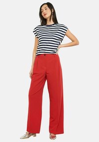 Varritudes sinise ja valge triibusega lühikeste varrukatega top, mida on kombineeritud kõrge vöökohaga punaste laiade pükstega. Modell kannab metallik-hõbedasi kingi.