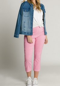 Jeansová bunda se dvěma náprsními kapsami, bílý uzlový tričko a růžové kára krátké kalhoty. Bílé tenisky dotvářejí outfit.