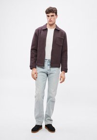 Tamnoljubičasta teksturirana jakna s ovratnikom i prednjim džepom, nošena preko bijele majice, uparena sa svijetloplavim trapericama i crnim cipelama.